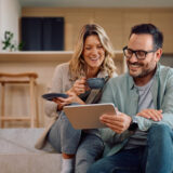 Happy couple using digital tablet while relaxing at home.