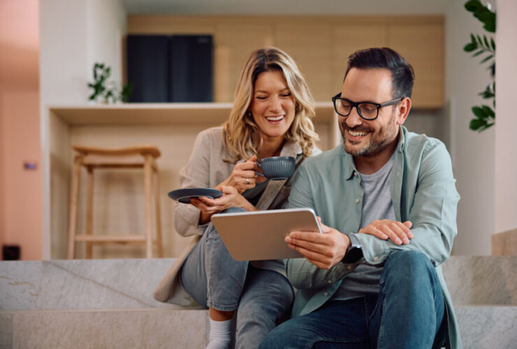 Happy couple using digital tablet while relaxing at home.